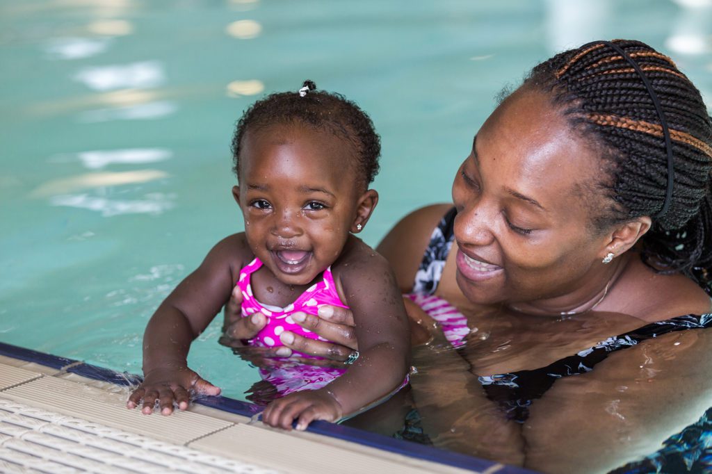 Infant,Swimming,Lessons,In,Indoor,Pool. African mother and daughter in a swimming pool
